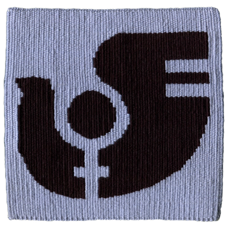 Imagen de un tapiz tejido a telar que reproduce el logotipo de la boletina feminista “Palomita”, que circuló en Chile entre 1985 y 1987. En la imagen vemos el logo tejido en negro sobre un donfo celeste.