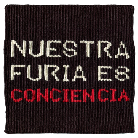 Imagen de un tapiz tejido a telar que reproduce la consigna “Nuestra furia es conciencia”. Imagen con fondo negro y textos en blanco y rojo.